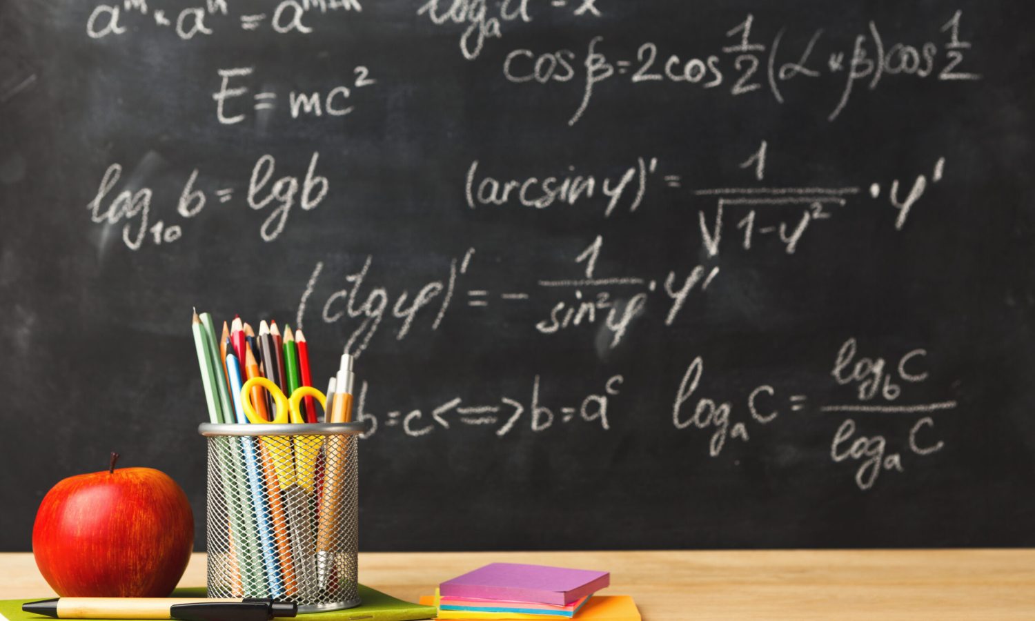 Studying mathematics educational background. Pencils, scissors and apple against classroom blackboard with chalk writing of sums. Back to school, research concept