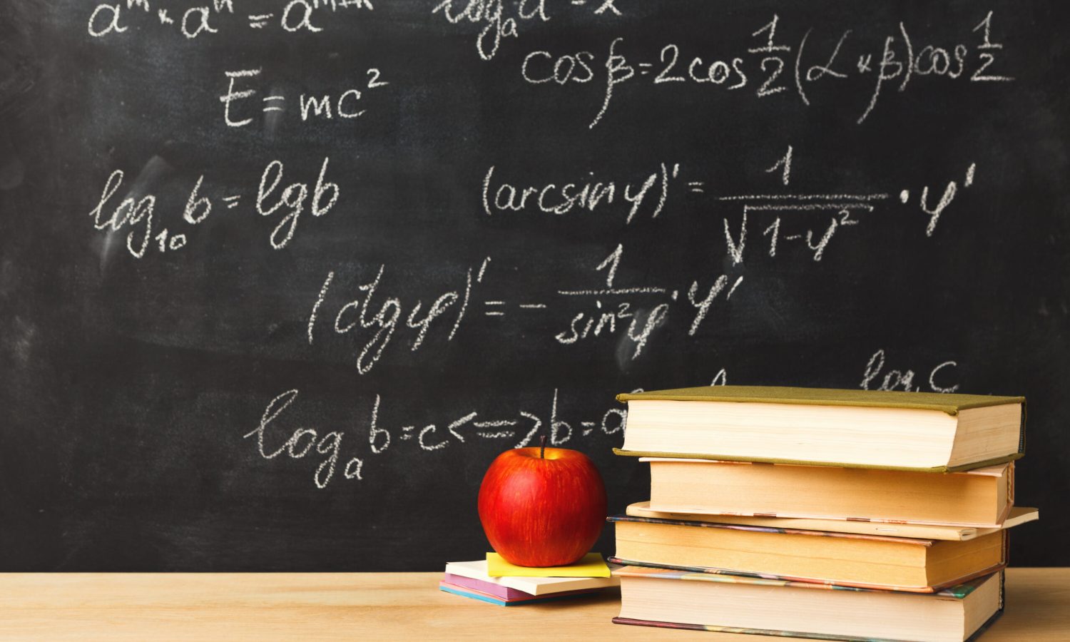 Studying mathematics educational background. Books pile and apple against classroom blackboard with chalk writing of sums. Back to school, research concept